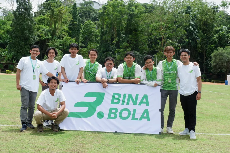 The BinaBola team behind a BinaBola banner on a football pitch in 2024, the year of Bangkit Academy.